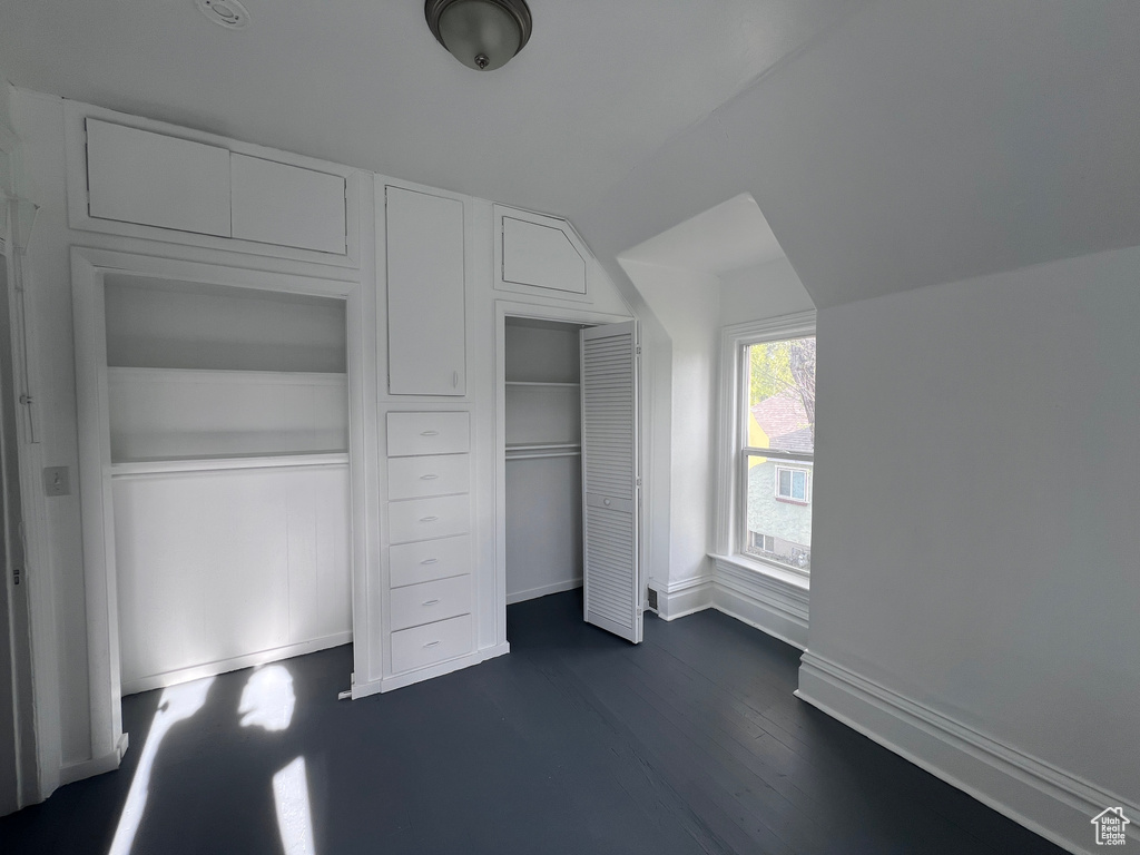 Unfurnished bedroom featuring baseboards, vaulted ceiling, dark wood-type flooring, and a closet
