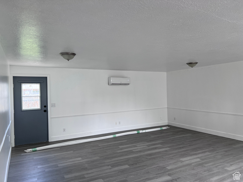 Empty room featuring a textured ceiling, a wall mounted air conditioner, and wood finished floors