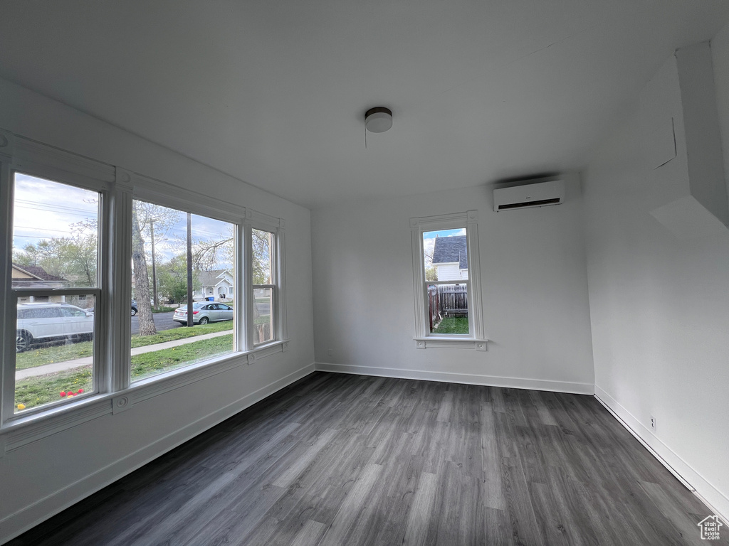 Unfurnished room featuring an AC wall unit, baseboards, dark wood finished floors, and a healthy amount of sunlight