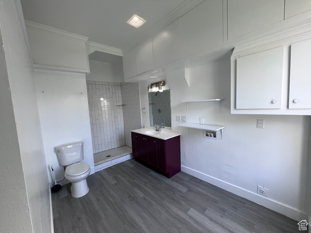 Full bathroom with vanity, toilet, wood finished floors, ornamental molding, and tiled shower