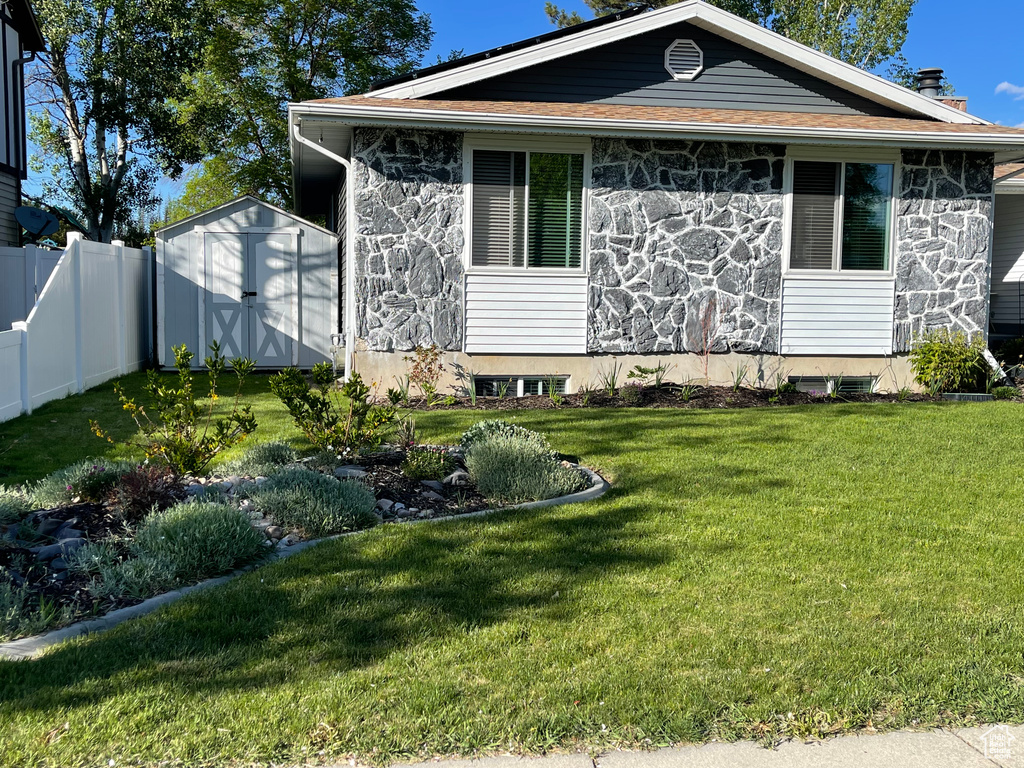 View of front of property featuring fence, a front yard, a shed, and stone siding