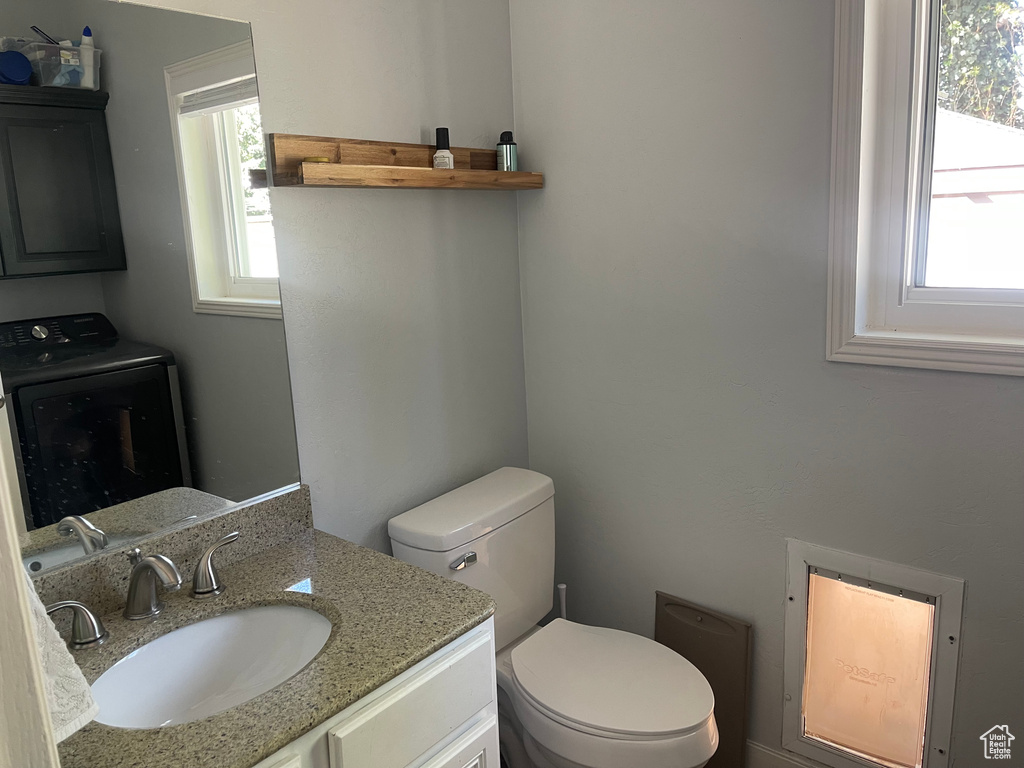 Half bathroom with vanity, toilet, washer / clothes dryer, and a wealth of natural light