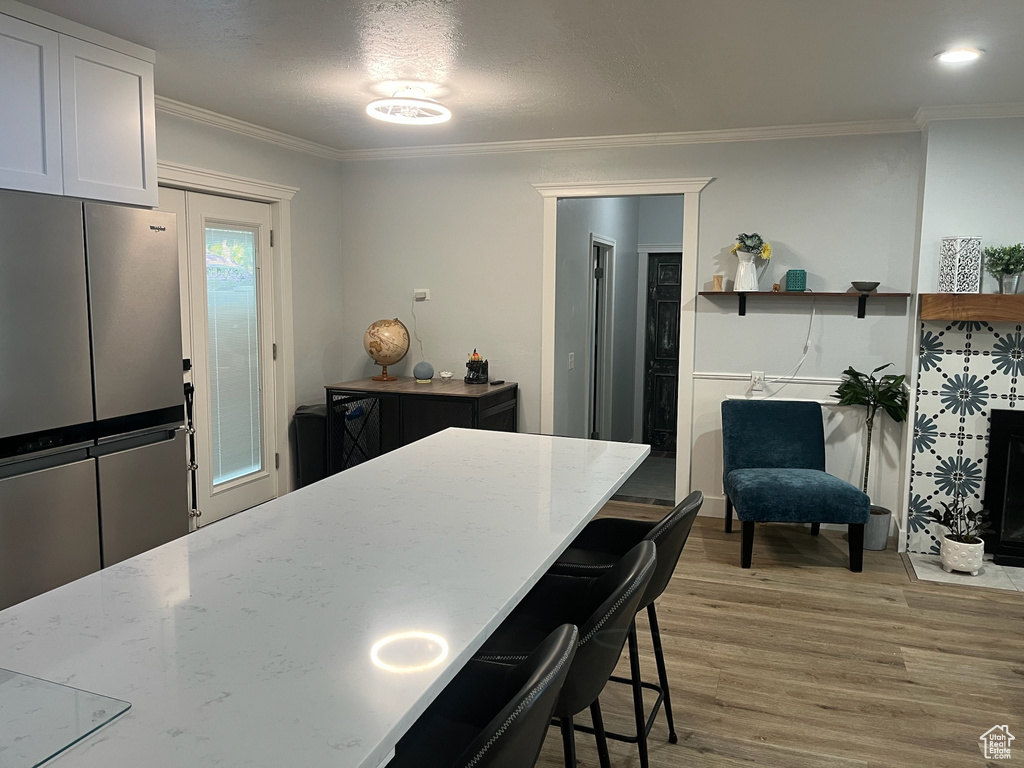Kitchen featuring light stone countertops, light wood-style floors, a kitchen breakfast bar, freestanding refrigerator, and ornamental molding