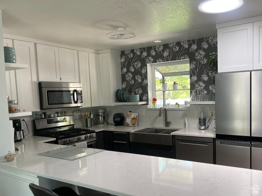 Kitchen featuring a kitchen bar, a sink, white cabinets, stainless steel appliances, and wallpapered walls