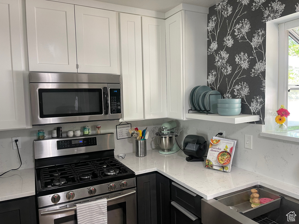 Kitchen featuring appliances with stainless steel finishes, white cabinets, and wallpapered walls