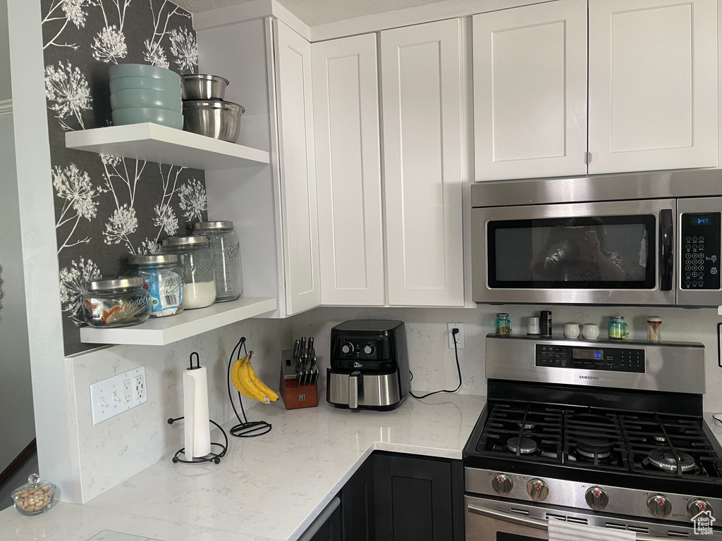 Kitchen with open shelves, light stone countertops, white cabinetry, backsplash, and stainless steel appliances