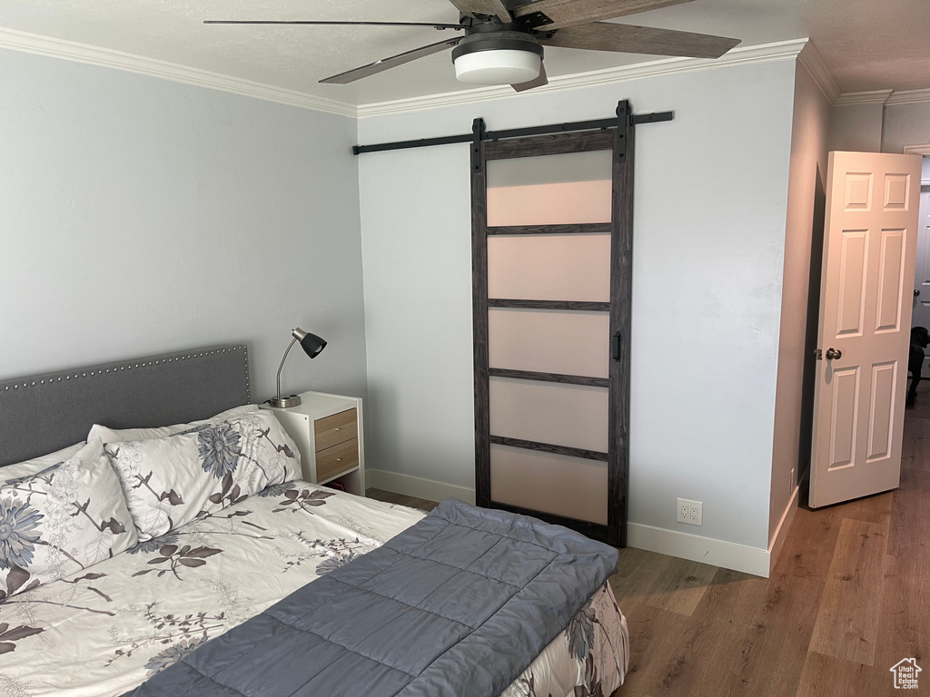 Bedroom featuring a ceiling fan, a barn door, wood finished floors, baseboards, and ornamental molding