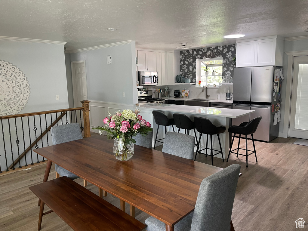 Dining area with crown molding, a wainscoted wall, light wood-type flooring, and a textured ceiling
