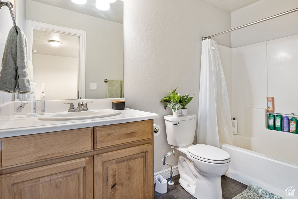 Full bath with vanity, toilet, wood finished floors, and shower / bath combination with curtain