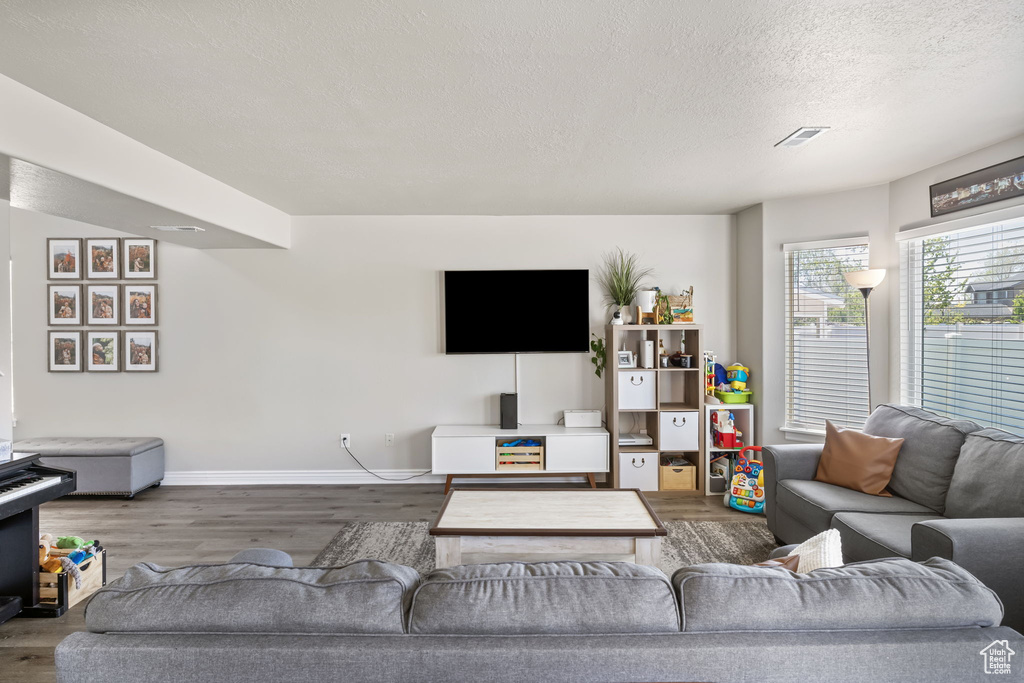 Living room featuring a textured ceiling, baseboards, wood finished floors, and visible vents