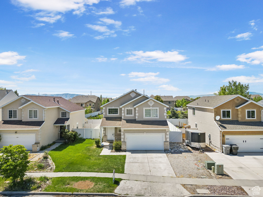 View of front facade featuring driveway, a front yard, a residential view, a garage, and fence