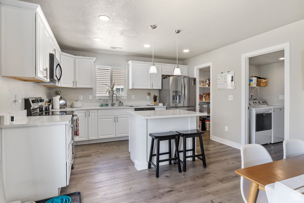 Kitchen featuring a kitchen bar, a sink, white cabinets, separate washer and dryer, and stainless steel appliances
