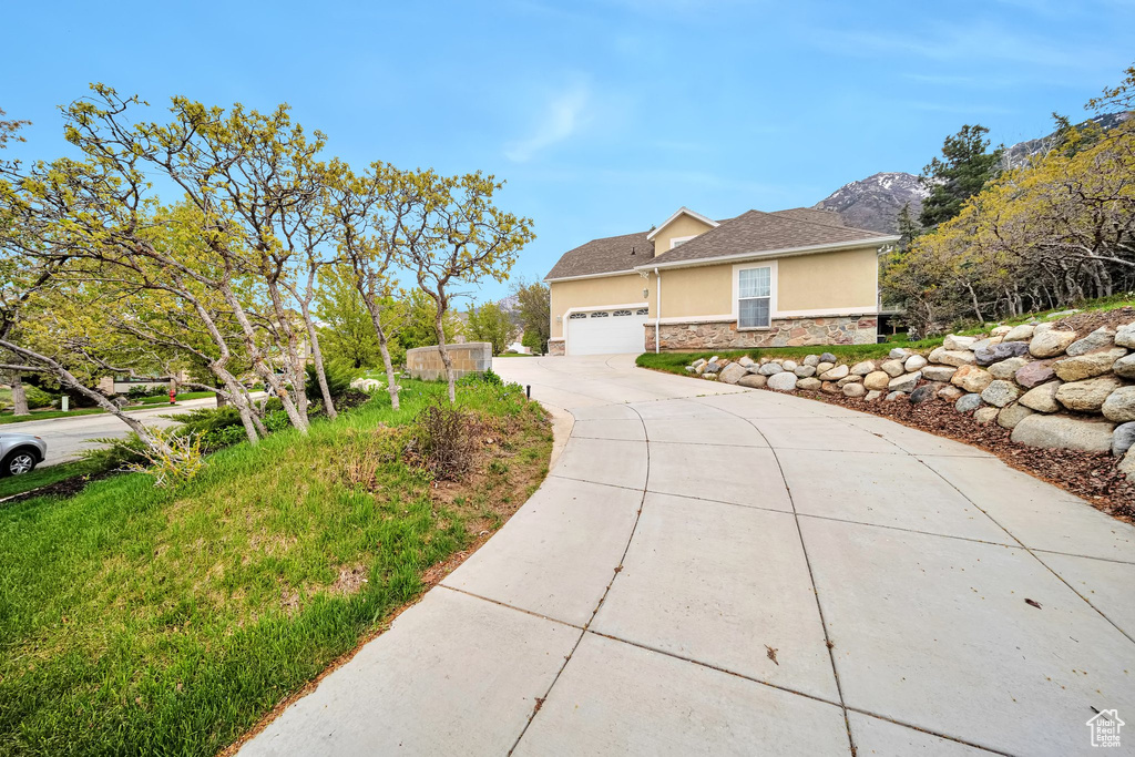 View of home's exterior with stucco siding, stone siding, a mountain view, concrete driveway, and an attached garage