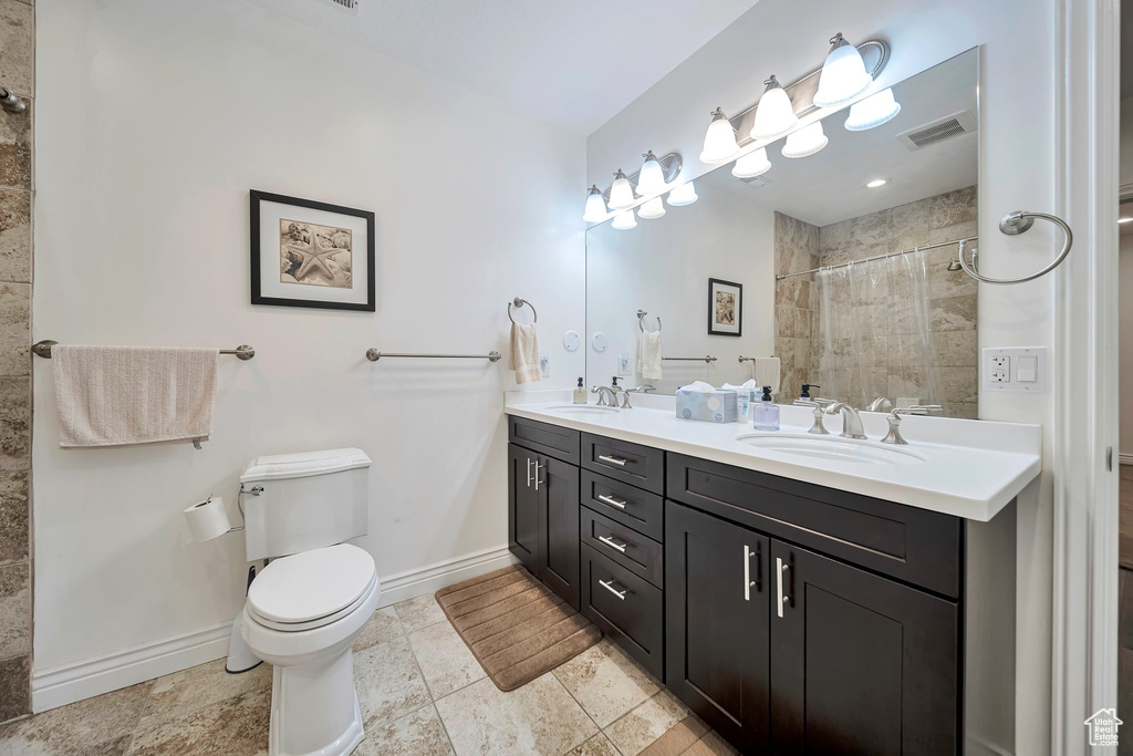 Full bathroom featuring a sink, tiled shower, toilet, visible vents, and baseboards