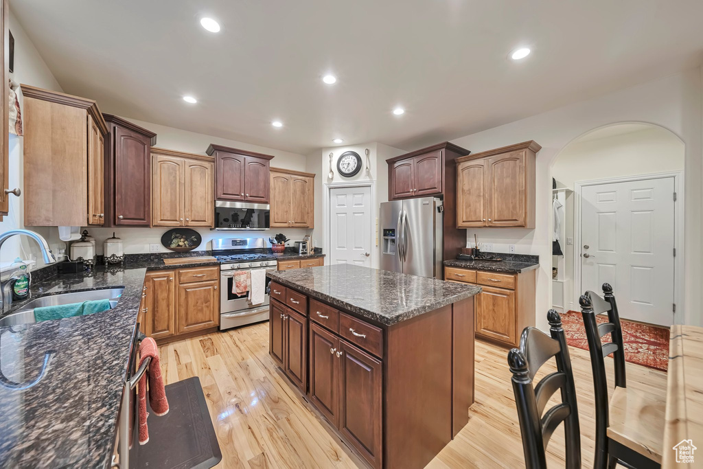 Kitchen with a sink, light wood-type flooring, a center island, arched walkways, and appliances with stainless steel finishes