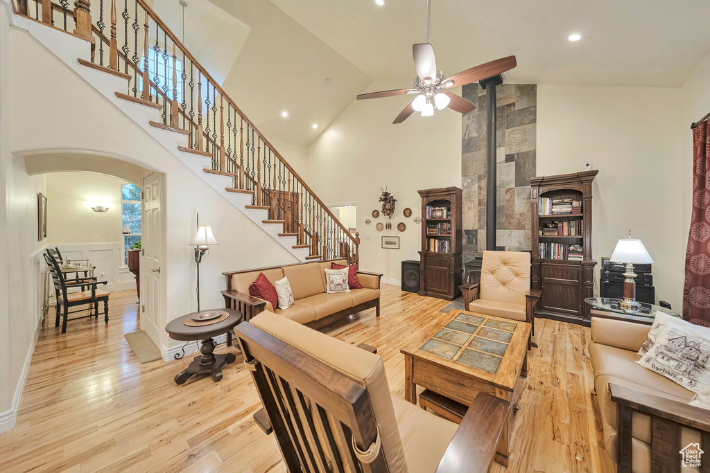 Living area with arched walkways, wood finished floors, stairway, high vaulted ceiling, and a ceiling fan