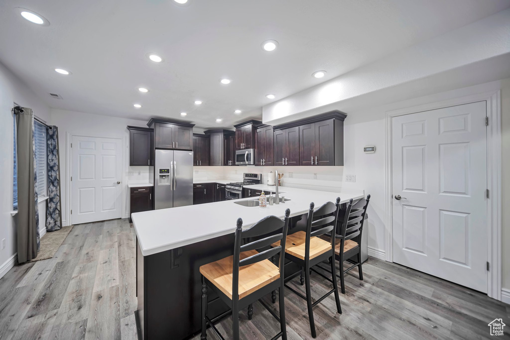 Kitchen with a kitchen breakfast bar, light wood-type flooring, a peninsula, light countertops, and appliances with stainless steel finishes
