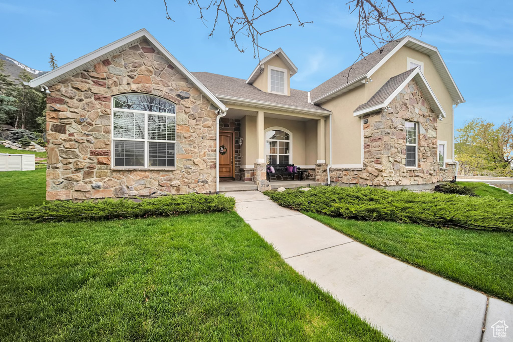 View of front of property with a front yard, stone siding, stucco siding, and covered porch