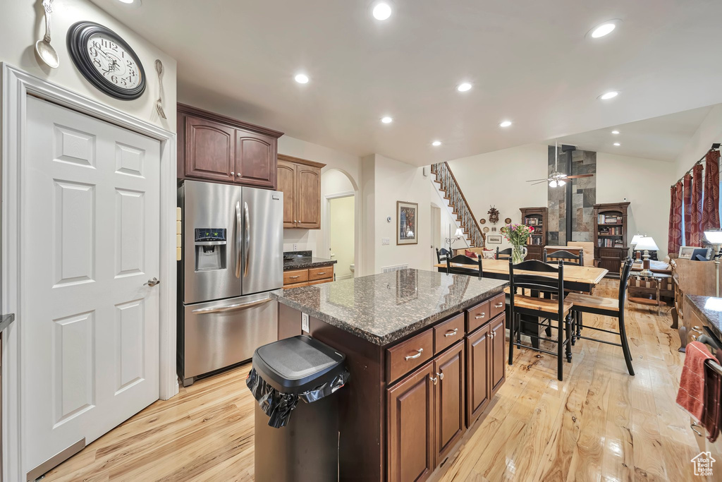 Kitchen featuring light wood finished floors, stainless steel fridge, a ceiling fan, a kitchen island, and arched walkways
