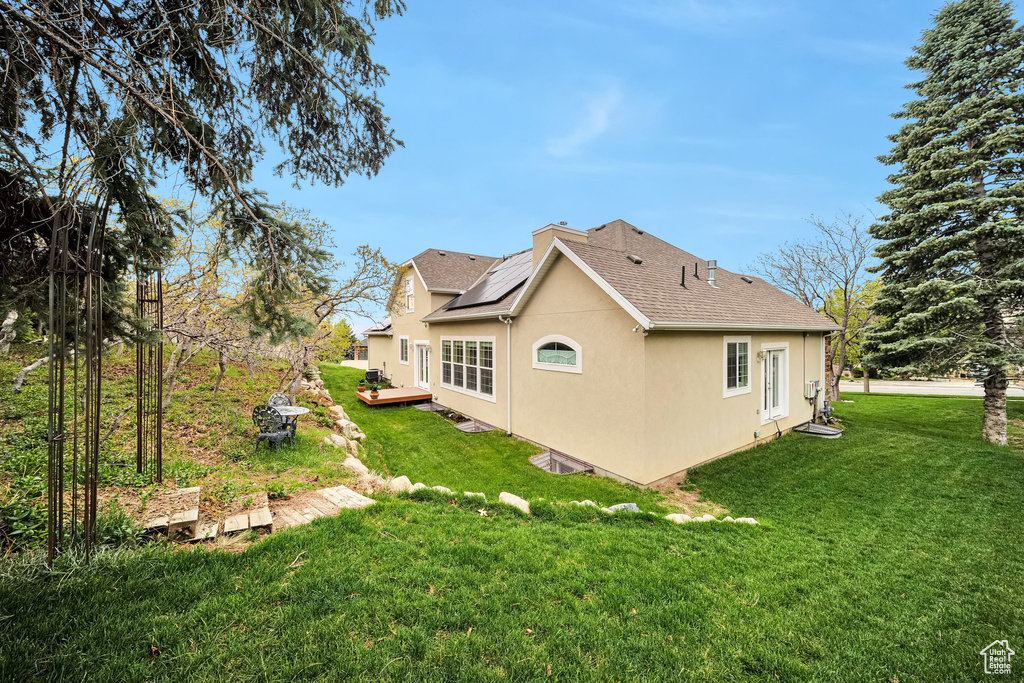 Back of property with a deck, stucco siding, a shingled roof, solar panels, and a lawn