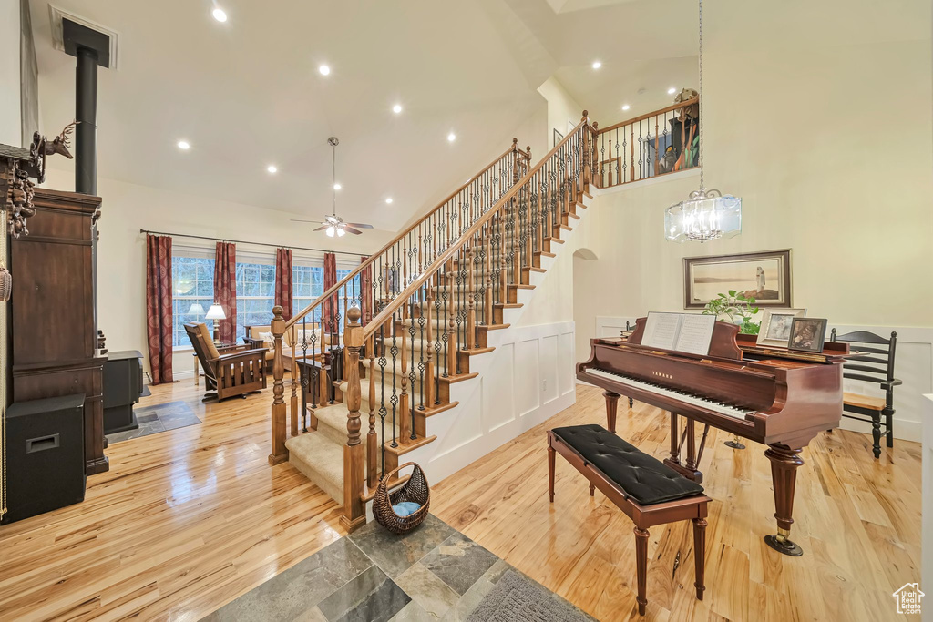 Stairs with wood finished floors, recessed lighting, a high ceiling, and ceiling fan with notable chandelier