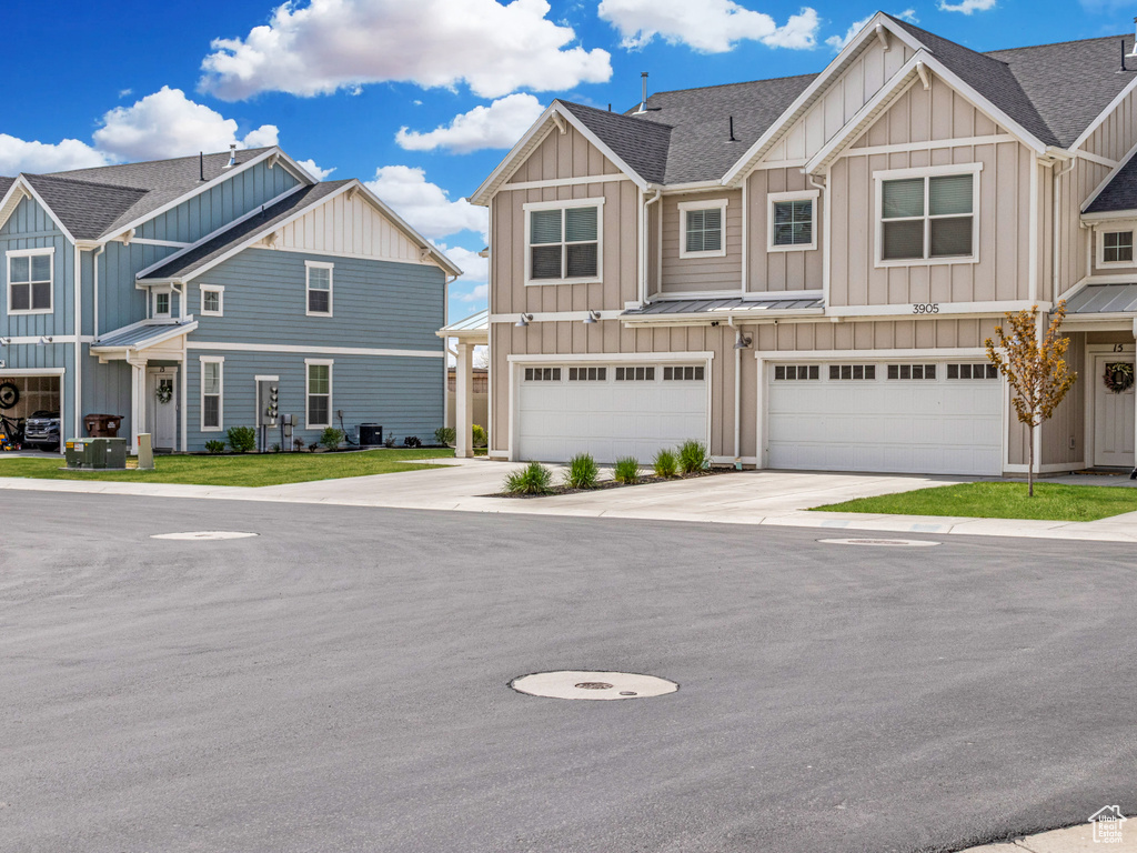 Townhome / multi-family property with roof with shingles, board and batten siding, driveway, and a garage