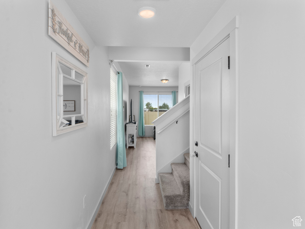 Hallway with light wood-type flooring, baseboards, and stairway