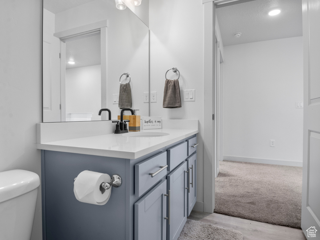 Half bathroom featuring recessed lighting, vanity, toilet, and wood finished floors