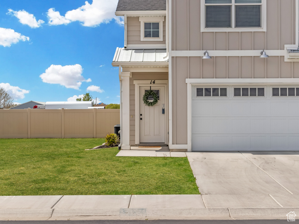 Entrance to property featuring fence, a garage, board and batten siding, a yard, and driveway