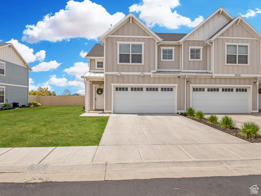 Townhome / multi-family property with board and batten siding, fence, a front yard, and a garage