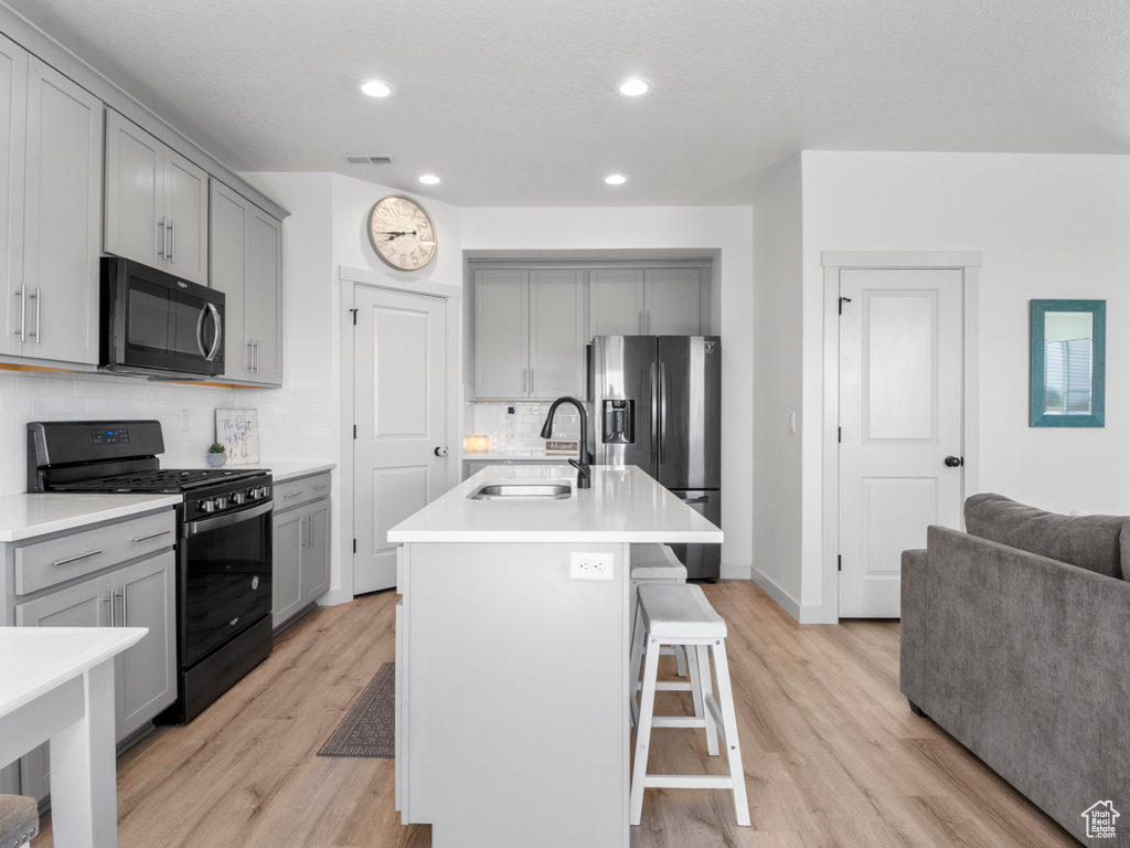 Kitchen with gray cabinetry, stainless steel fridge, and gas range oven