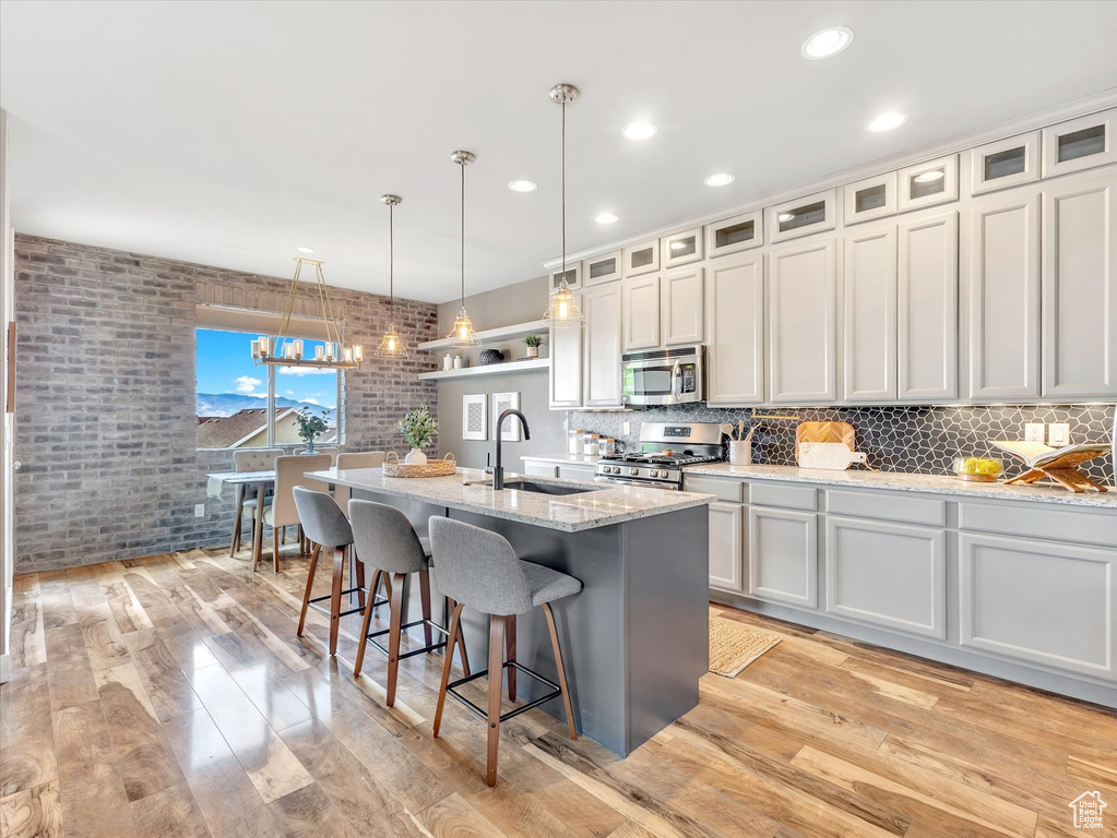 Kitchen with a kitchen island with sink, a kitchen bar, a sink, light wood-style floors, and stainless steel appliances