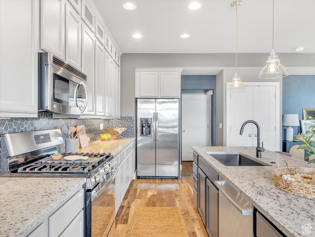 Kitchen with white cabinetry, appliances with stainless steel finishes, a sink, and light wood-type flooring
