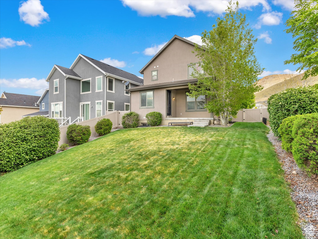 Back of property featuring a lawn, a fenced backyard, stucco siding, and a gate