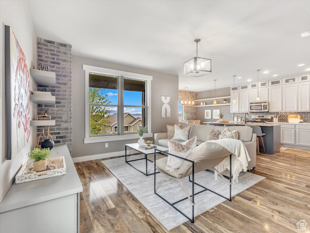 Living room with light wood-type flooring, baseboards, a notable chandelier, and a healthy amount of sunlight