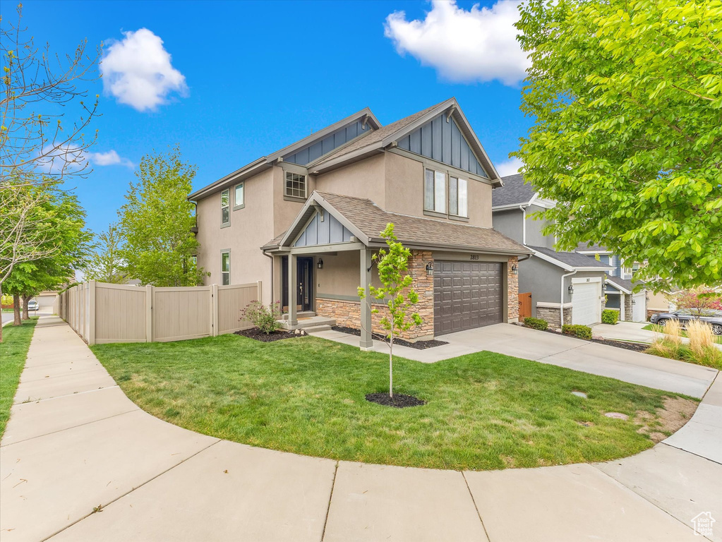 View of front of home featuring fence, an attached garage, stone siding, stucco siding, and a front yard