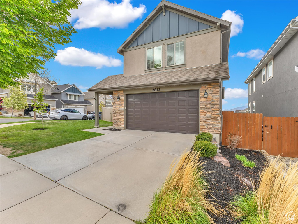 View of front of property featuring board and batten siding, an attached garage, driveway, and stone siding