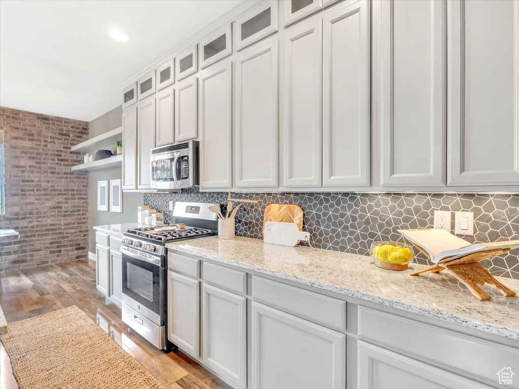 Kitchen featuring open shelves, appliances with stainless steel finishes, light stone counters, light wood finished floors, and tasteful backsplash