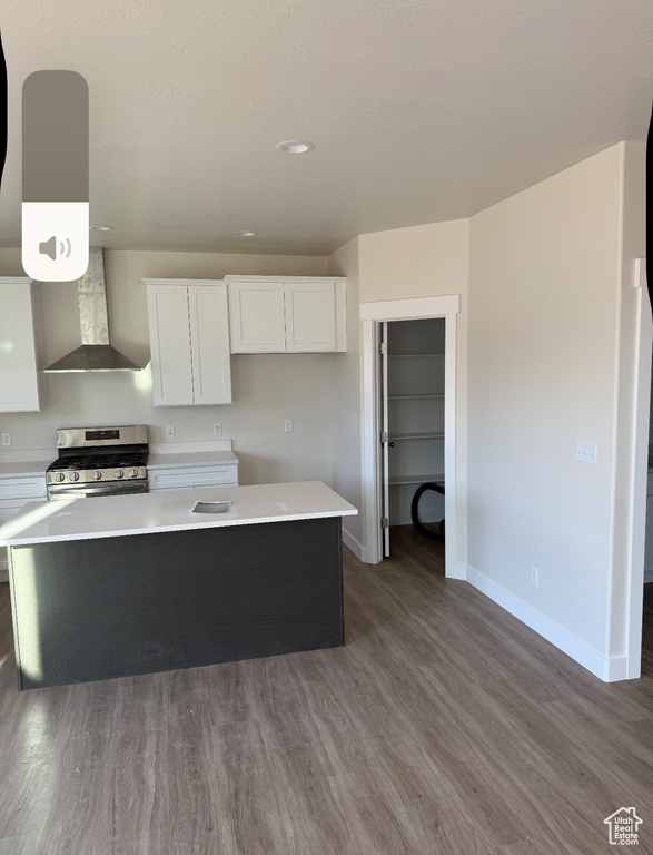 Kitchen featuring dark wood-style flooring, stainless steel range with gas stovetop, wall chimney exhaust hood, white cabinetry, and baseboards