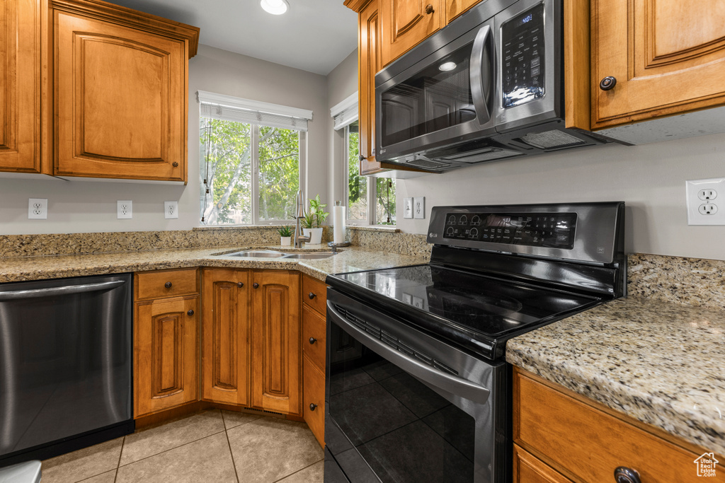 Kitchen with light tile patterned floors, appliances with stainless steel finishes, brown cabinetry, and a sink