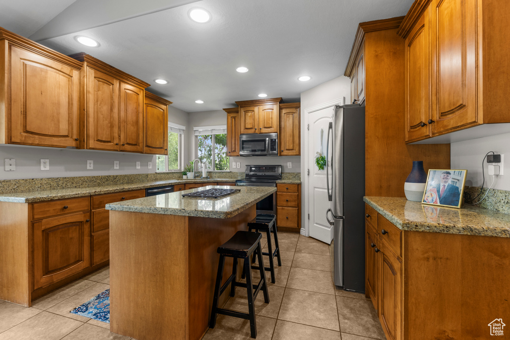 Kitchen with brown cabinetry, a kitchen breakfast bar, a center island, a sink, and appliances with stainless steel finishes