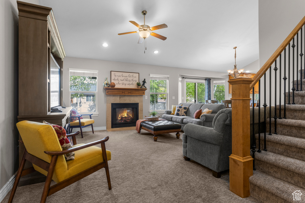 Carpeted living area with baseboards, stairway, recessed lighting, a tiled fireplace, and ceiling fan with notable chandelier