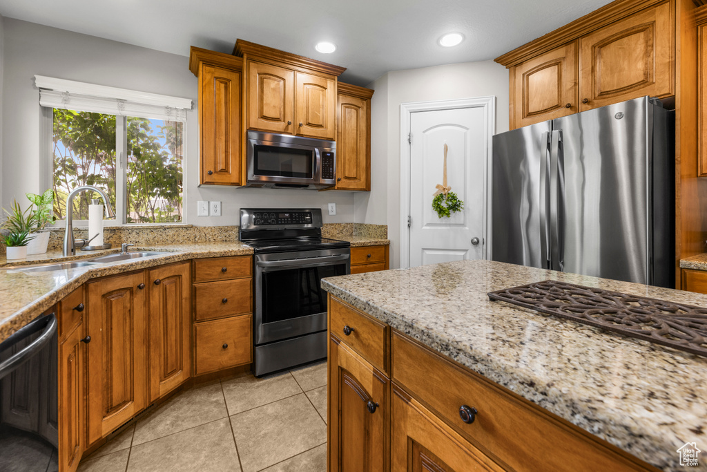 Kitchen featuring brown cabinetry, light stone countertops, a sink, stainless steel appliances, and light tile patterned flooring