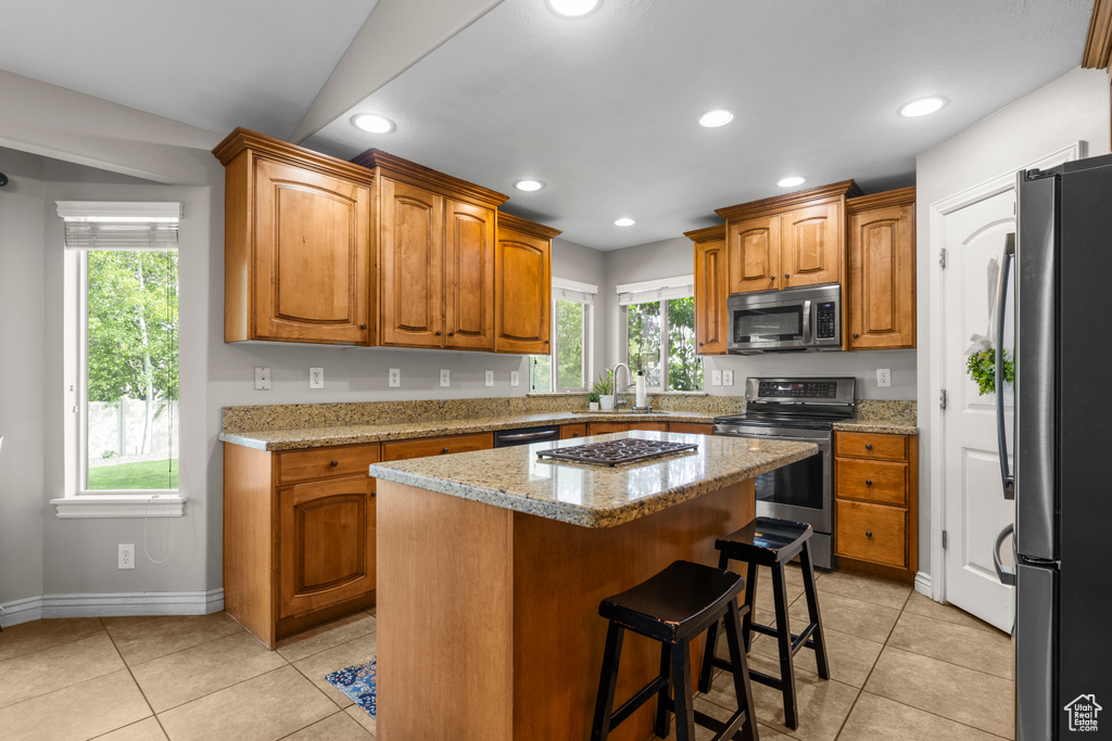 Kitchen with a sink, appliances with stainless steel finishes, brown cabinets, and light tile patterned flooring