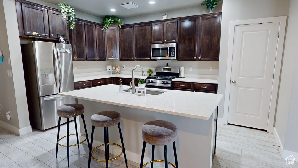 Kitchen featuring appliances with stainless steel finishes, dark brown cabinets, a breakfast bar area, an island with sink, and recessed lighting