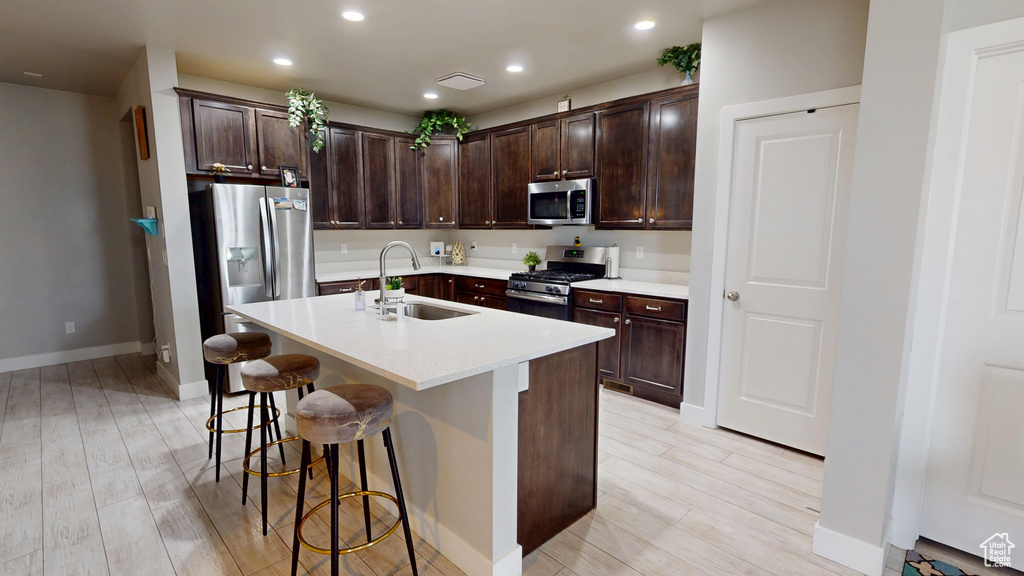 Kitchen with appliances with stainless steel finishes, dark brown cabinets, a breakfast bar, an island with sink, and recessed lighting