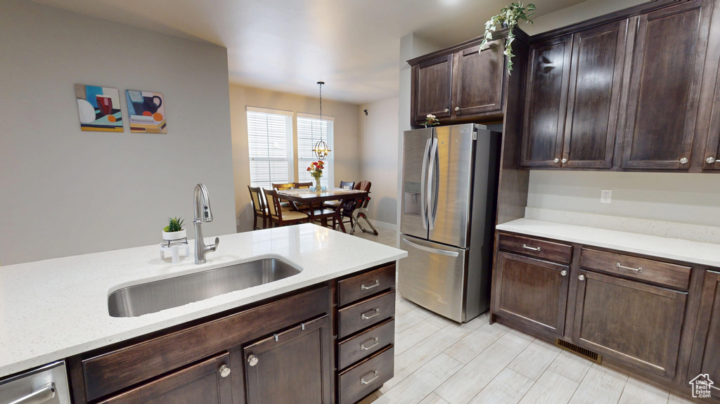 Kitchen featuring dark brown cabinets, light wood-type flooring, stainless steel fridge with ice dispenser, a sink, and hanging light fixtures