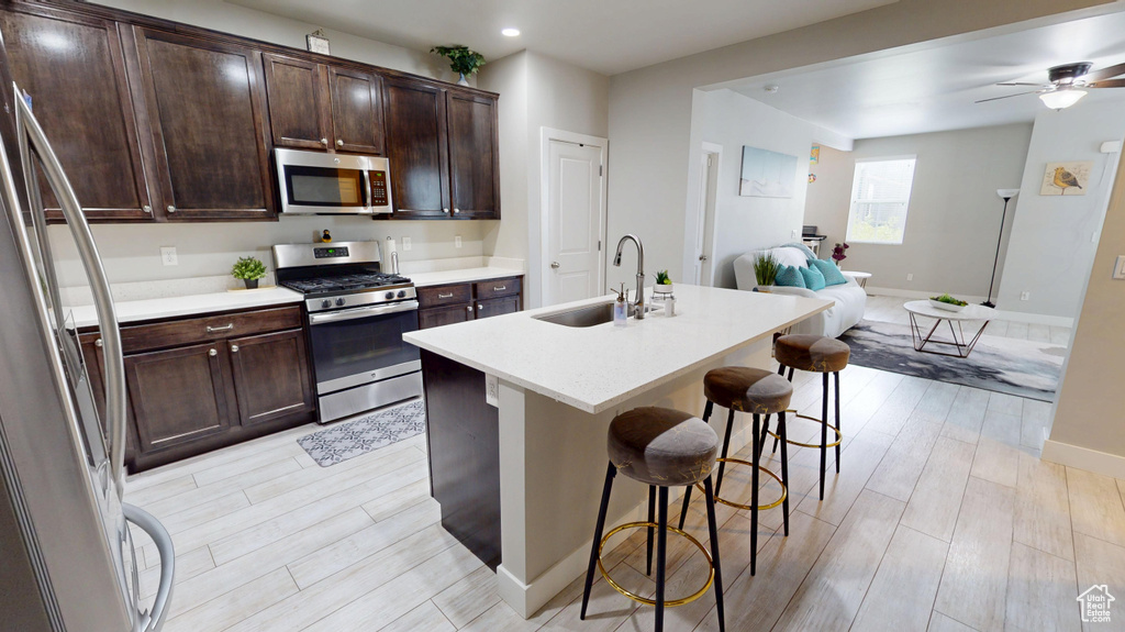 Kitchen featuring stainless steel appliances, open floor plan, light wood finished floors, a breakfast bar area, and recessed lighting