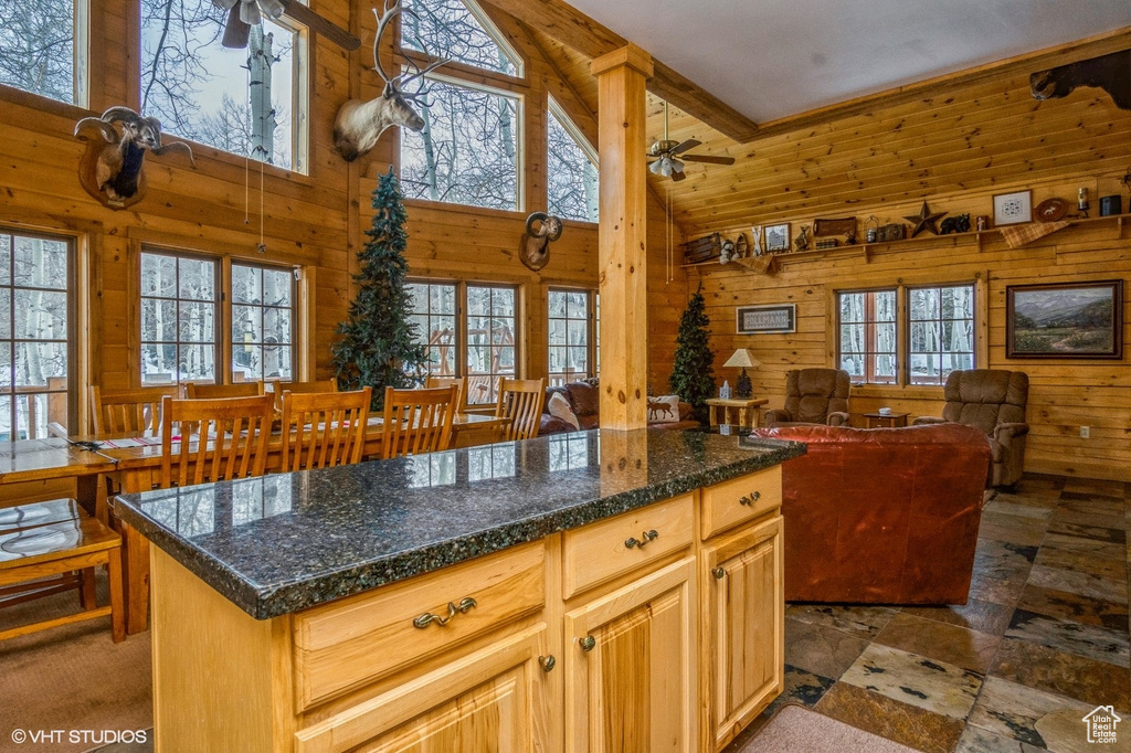 Kitchen featuring wood walls, dark countertops, open floor plan, ceiling fan, and high vaulted ceiling