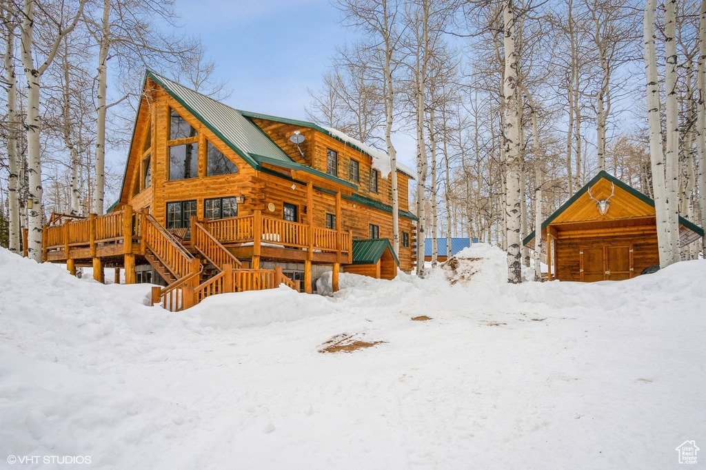 Snow covered rear of property with a wooden deck, log exterior, and metal roof